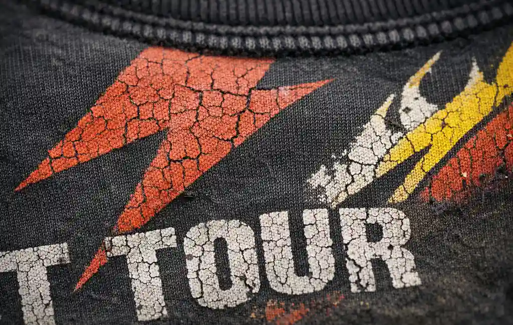 Close-up detail of cracked screen print on a faded 90s band shirt graphic.